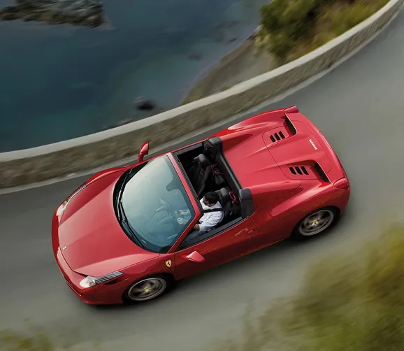Red Ferrari 458 Spider seen from above sweeping through a coastal mountain bend