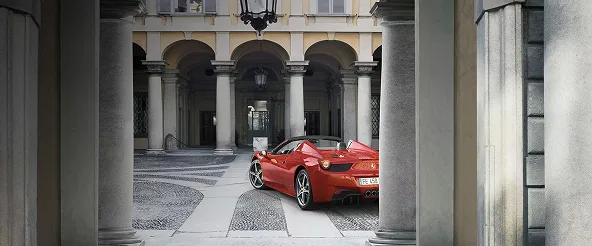 Red Ferrari 458 Spider parked in a stone courtyard beneath an arched colonnade