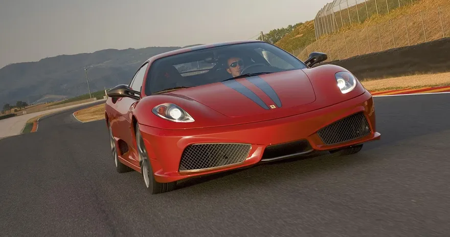 Red Ferrari F430 Scuderia at speed on a circuit with the driver visible through the windscreen