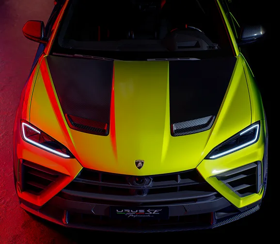 Front view of a lime green Lamborghini Urus with its angular headlights lit
