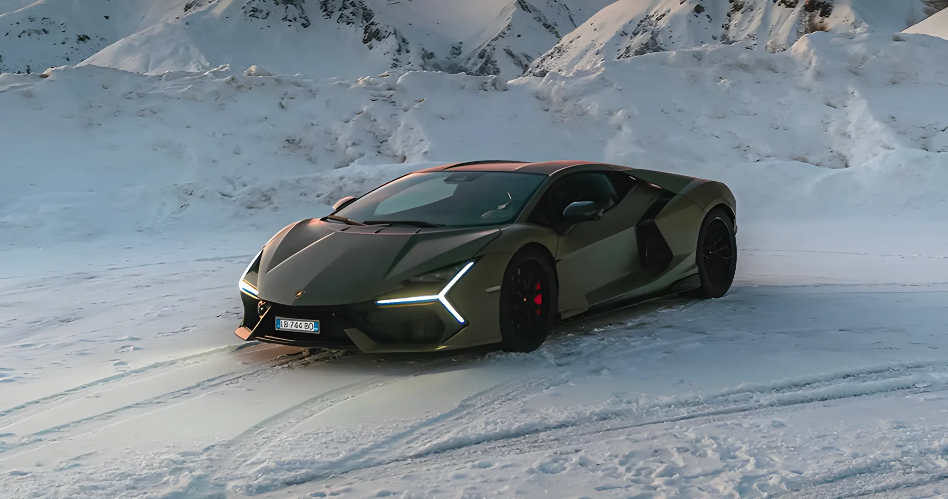 Dark green Lamborghini Revuelto on a snow-covered mountain road at sunset