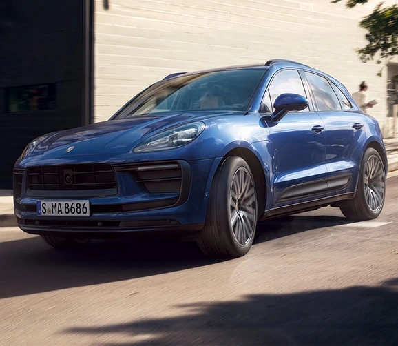 Blue Porsche Macan driving past a sunlit wall